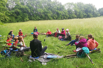 Kinder sitzen im Kreis auf der Wiese und hören eine Geschichte von Fabelwesen